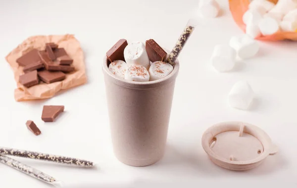 reusable coffee cup with marshmallows and chocolate on a white plate next to the ingredients