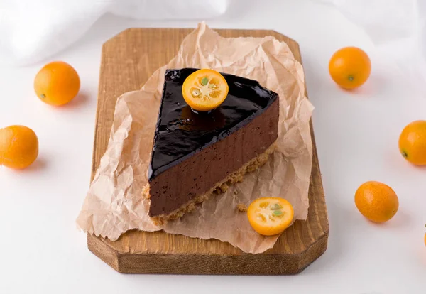 Bolo de chocolate com cacau em uma placa de madeira decorada com kumquat de frutas cítricas em um fundo branco. ao lado da sobremesa são frutas frescas — Fotografia de Stock