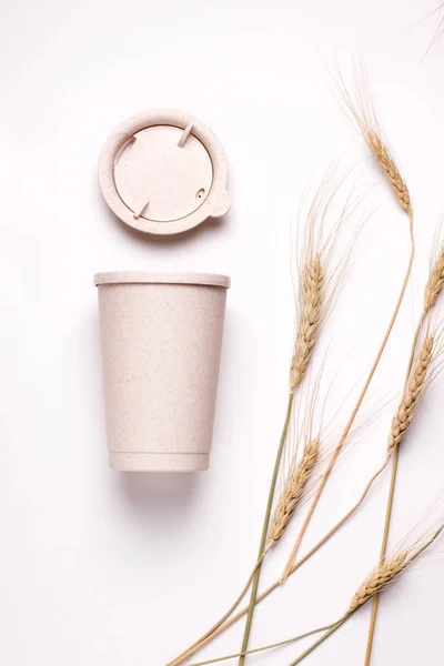 Taza de café reutilizable de paja sobre un fondo blanco junto a espiguillas. imagen vertical —  Fotos de Stock