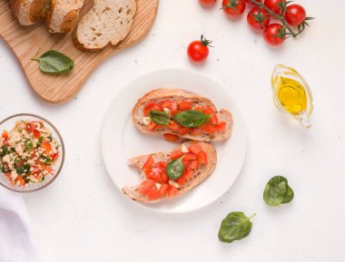 Ekmek ve zeytinyağının yanında beyaz tabakta domatesli bruschetta sandviçi, bulgur ve maydanoz salatası ile vejetaryen kahvaltısı.