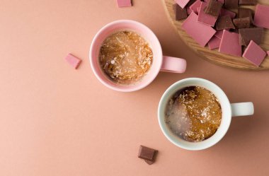 Kahverengi arka planda sütlü iki fincan kahve, çikolatanın yanında. Boşluğu kopyala