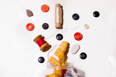 Farklı renklerdeki düğmeler ve iplikler beyaz arka plandaki kutudan dökülüyor. Eski şeyleri tamir etme ve dikiş dikme konsepti