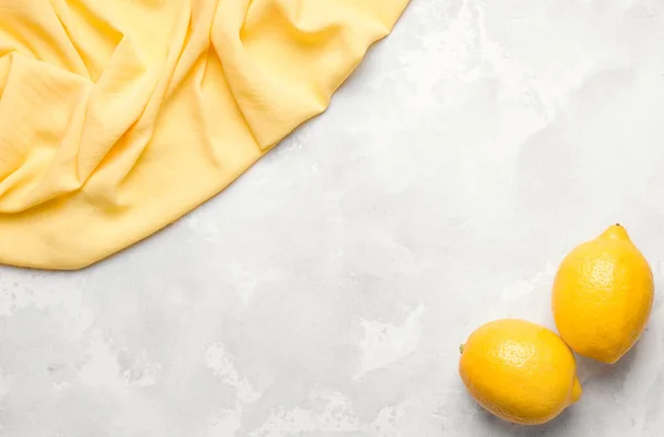 Somut gri arka plan, sarı bez ve limonlar. Boşluğu kopyala