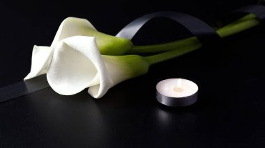 White Zantedesia with mourning ribbon and burning candles on a black background. Concept of sorrow and death clipart