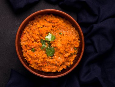 Siyah arka planda kişniş soslu geleneksel vejetaryen kırmızı mercimek çorbası..