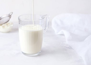 Fermente edilmiş süt kefir beyaz arka planda bir bardağa dökülür..