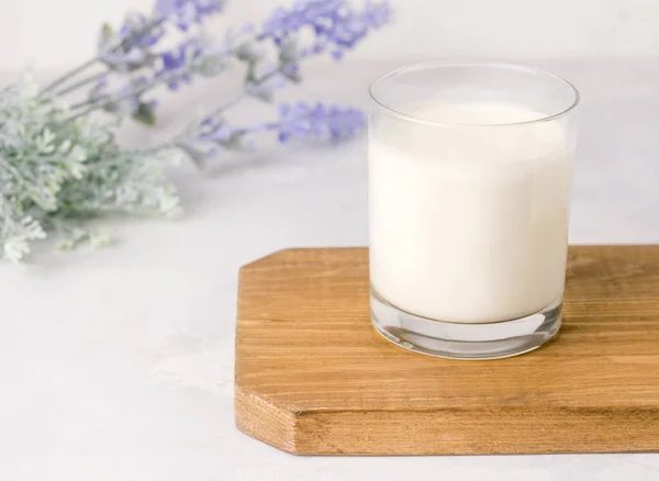 Beyaz bir arka planda tahta bir tahtanın üzerinde bir bardakta mayalanmış kefir içeceği. Kırsal