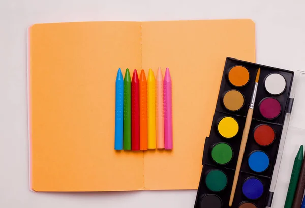 The concept of drawing lessons. Crayons and paints of different colors lie on a notebook