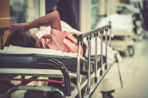 Görüntü hastanesinin arka planında yaşlı bir hasta yatıyor ve tekerlekli sandalye bekleme koridorunda bekliyor. Profesyonel hemşire ve doktorun desteğiyle hasta insanlar için kötü sağlık hizmeti 