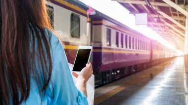 Tren platformundaki genç sırt çantalı turist internetteki wi-fi arama kılavuzu bilgilerini kullanıyor ucuz indirimli tanıtım kitabı otobüs otobüs bileti Coronavirus karantinasından sonra otel uçuşu