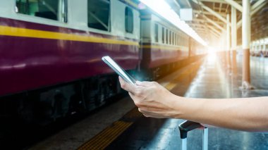 Tren platformundaki genç sırt çantalı turist internetteki wi-fi arama kılavuzu bilgilerini kullanıyor ucuz indirimli tanıtım kitabı otobüs otobüs bileti Coronavirus karantinasından sonra otel uçuşu