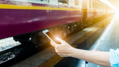 Tren platformundaki genç sırt çantalı turist internetteki wi-fi arama kılavuzu bilgilerini kullanıyor ucuz indirimli tanıtım kitabı otobüs otobüs bileti Coronavirus karantinasından sonra otel uçuşu