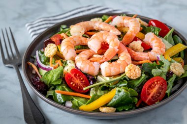 Mermer zemin üzerinde karides, domates, havuç, soğan, biber ve karışık yeşillik (roka, bahar karışımı) ve çatal ve çizgili peçeteyle taze salata. Sağlıklı yiyecekler. Temiz yemek. Keto.