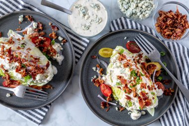 Mavi peynirli salata soslu buzdağı salatası, pastırma, domates, soğan, yukarıdan atılmış gri taş kaplar üzerinde duran soğanlar. Keto diyet dostu