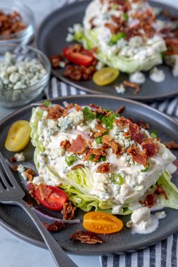 Klasik buzlu marul salatası üzerine mavi peynir sosu, pastırma, domates, soğan serpiştirilmiş gri tabaklar ve yanında malzemeler var. Dikey. Keto.