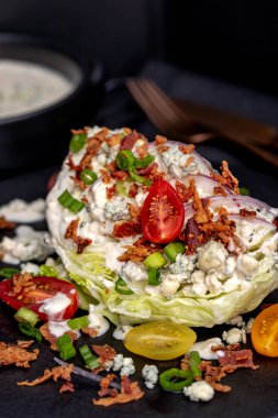 Klasik restoranın buz dağı salatasına mavi peynir sosu, pastırma, domates, soğan serpiştirilmiş salata sosu yanında da siyah tabakta duran soğan. Dikey. Keto.