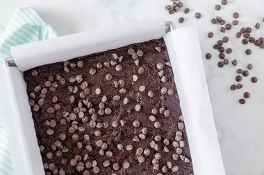 Keto çikolatalı browni hamuru metal fırın tavasında. Parşömen kağıdıyla kaplanmış. Çikolata parçacıkları fırın için hazır.