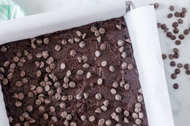 Çikolata parçalı çikolatalı kek hamuru, üzerinde çikolata parçacıkları olan parşömen kâğıdıyla kaplanmış metal fırın tavasında fırın için hazır.