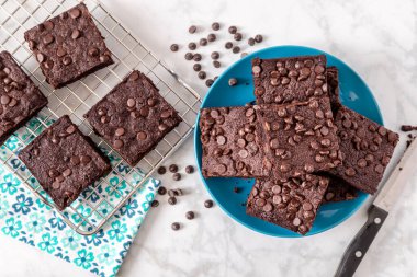 Keto chocolate chip brownies sitting on bright blue plate with additional brownies on baking rack with flower napkin clipart