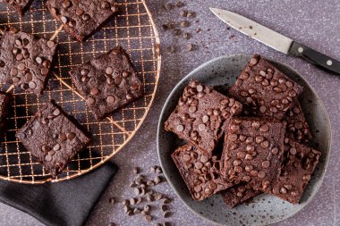 Gri taş tabakta keto çikolatalı kek yığını. Bakır fırın rafında da browni var.