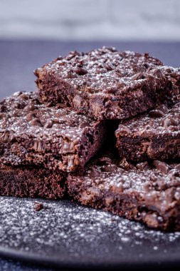 Stack of keto chocolate chip brownies sprinkled with powdered sugar against white brick background clipart