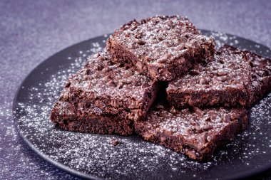 Kestaneli çikolatalı browni yığınını kapatıyoruz, üzerine toz şeker serpiştirilmiş, siyah taş kapta oturuyoruz.