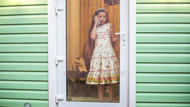 Дівчина біля дверей розмовляє по телефону, йде дощ — стокове відео