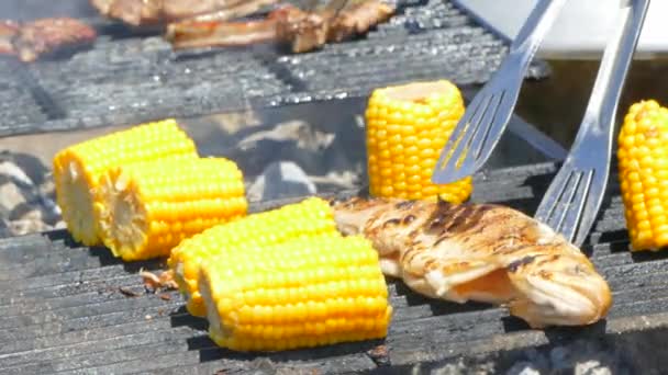 Повар печет рыбу и кукурузу на гриле — стоковое видео