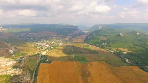 Landskap flygresa genom fältet och byn till bergen — Stockvideo