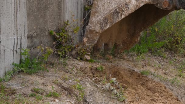 Excavator bucket cleans the ground next to the wall — Stock Video