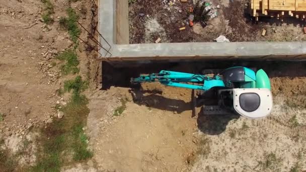 Een kleine blauwe graafmachine werkt in de buurt van het gebouw. Birds eye view. — Stockvideo