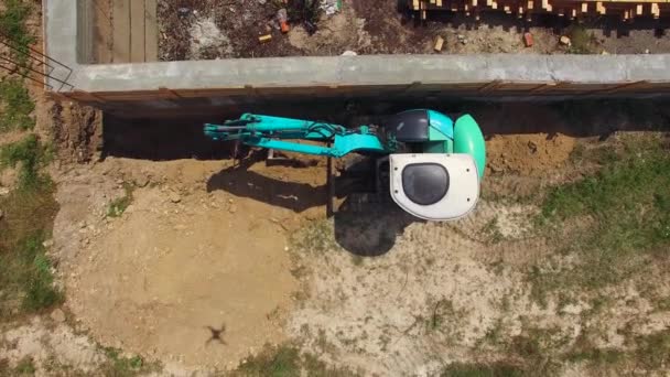 A small excavator works next to an unfinished building. birds eye view. — Stock Video