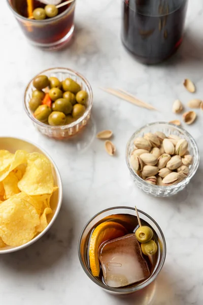Kırmızı vermut, zeytin, şam fıstığı ve cips içeren aperatif. Mermer tablo