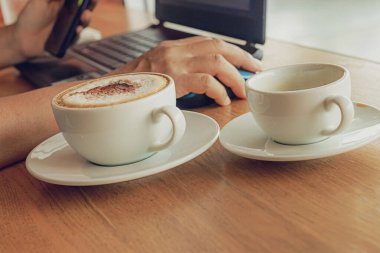 Kahve fincanları ve dizüstü bilgisayarla bir kafede çalışan serbest çalışan biri..