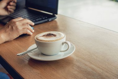 Kahve fincanları ve dizüstü bilgisayarla bir kafede çalışan serbest çalışan biri..