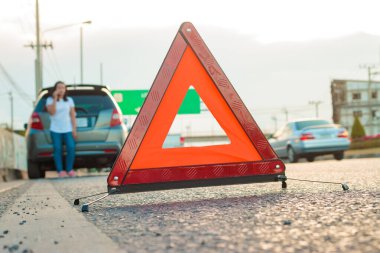 Asyalı genç kadınlar ellerinde cep telefonuyla arabanın etrafında dolaşıyorlar, akşam saatlerinde stresli bir ruh hali var. Otoyol boyunca çünkü arabası bozuldu ve birinden yardım bekliyor..