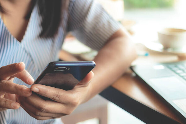 Женщина печатает текстовые сообщения на смартфоне в кафе. 