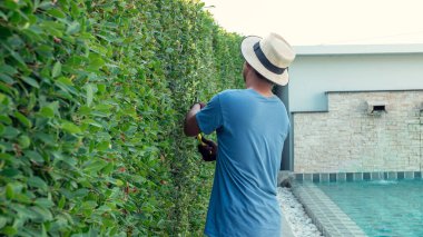 Bir adam evin bahçesinde dalları buduyor..