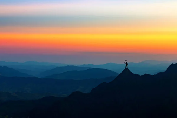 Business man with a victory flag on the hilltop at sunset, Concept of success