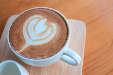 Sabahları, kahve dükkanındaki ahşap masada latte sanatıyla kahve fincanı..