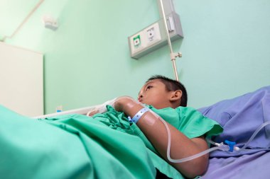 Asyalı bir çocuk hastane yatağında bir hastayı tedavi ediyor..