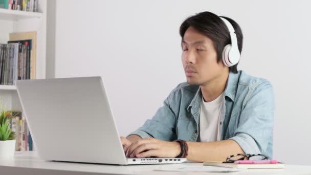 亚洲临时商人或自由职业者头戴耳机听音乐 在家里用笔记本电脑工作 — 图库视频影像