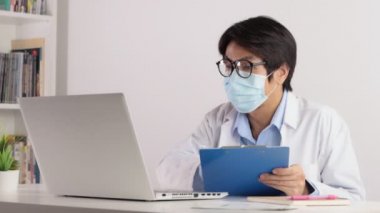 Asyalı Doktor Maske Giyer ve Gözlük Çevrimiçi İş Arkadaşlarıyla Dizüstü bilgisayarla Buluşma. Asyalı doktor dizüstü bilgisayarı ciddi duygularla izliyor