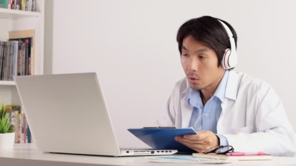 Asiatiska Manliga Läkare Bär Hörlurar Rapport Som Fungerar Med Laptop — Stockvideo