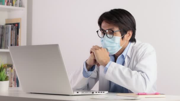 アジア男性医師摩耗マスクと白いコートやガウンをオンライン会議は 深刻な感情でビデオ会議ノートパソコンを渡す — ストック動画