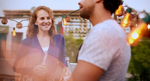 Multi-ethnic millenial couple flirting while having a drink on rooftop patio at sunset — Stock Photo, Image