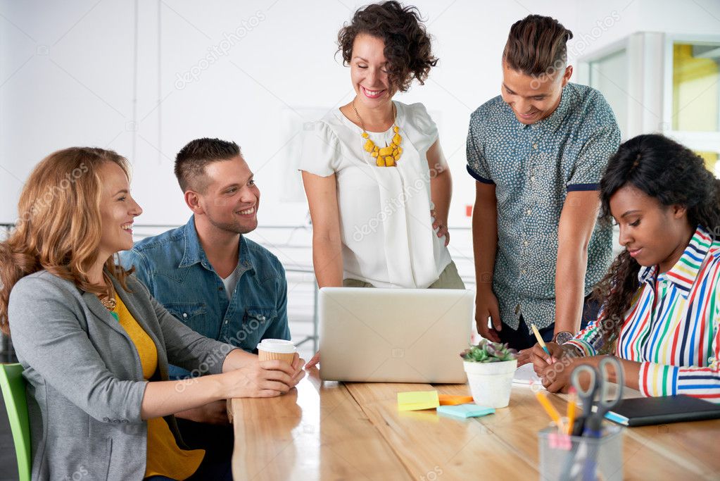 Multi ethnic group of succesful creative business people using a laptop during candid meeting