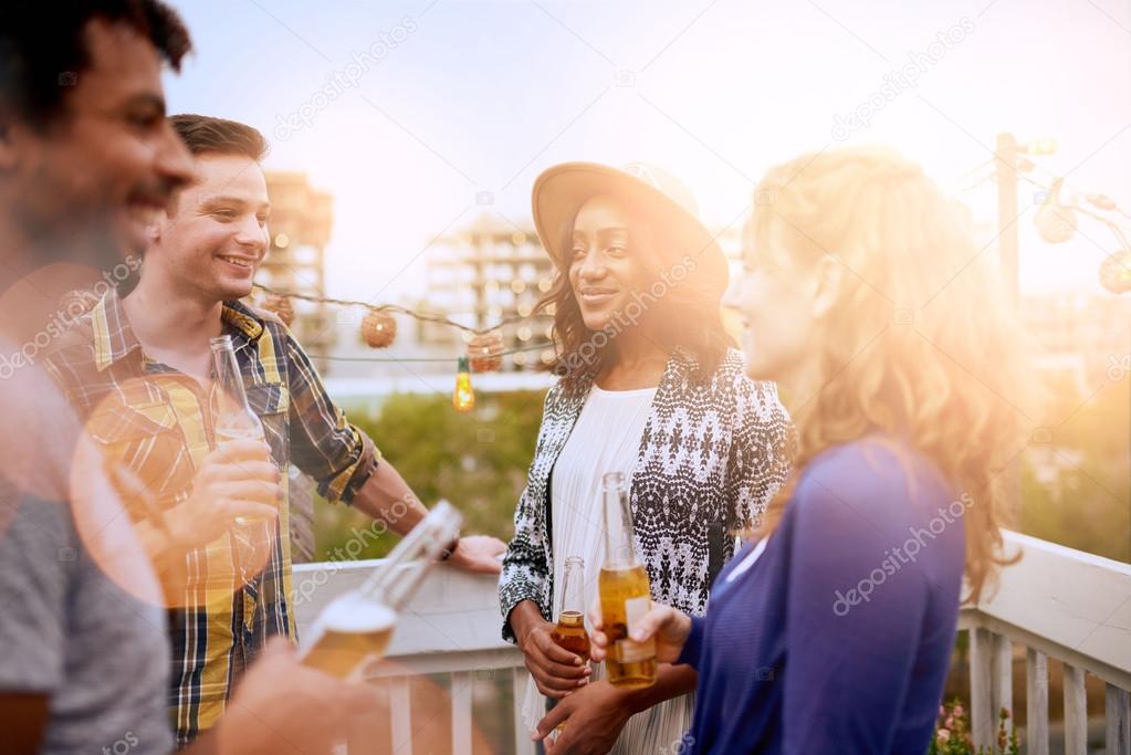 Multi-ethnic millenial group of friends partying and enjoying a beer on rooftop terrasse at sunset