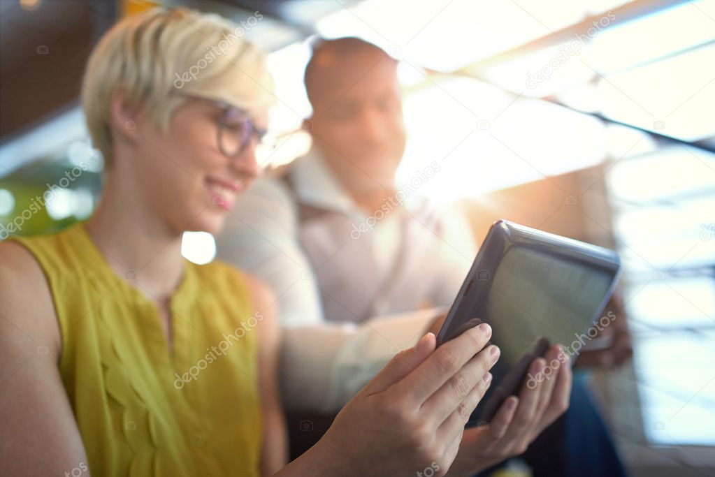 Two creative millenial small business owners working on social media strategy using a digital tablet while sitting in staircase