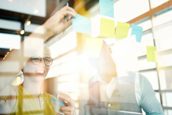 Dos propietarios de pequeñas empresas milenarias creativas que trabajan en una lluvia de ideas de estrategia de redes sociales utilizando notas adhesivas en ventanas — Foto de Stock